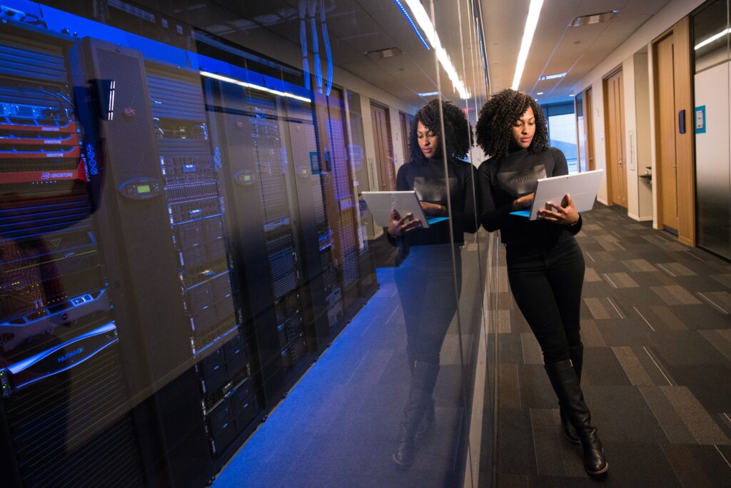 woman in black top standing next to server room using laptop