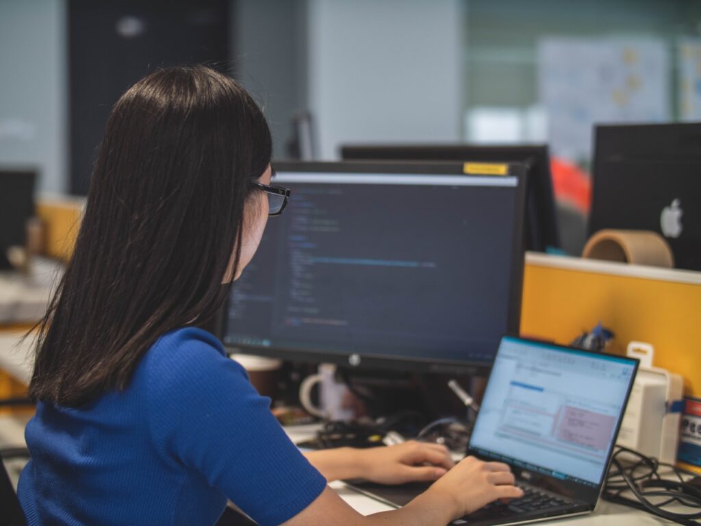 female working on her laptop with code showing on the monitor