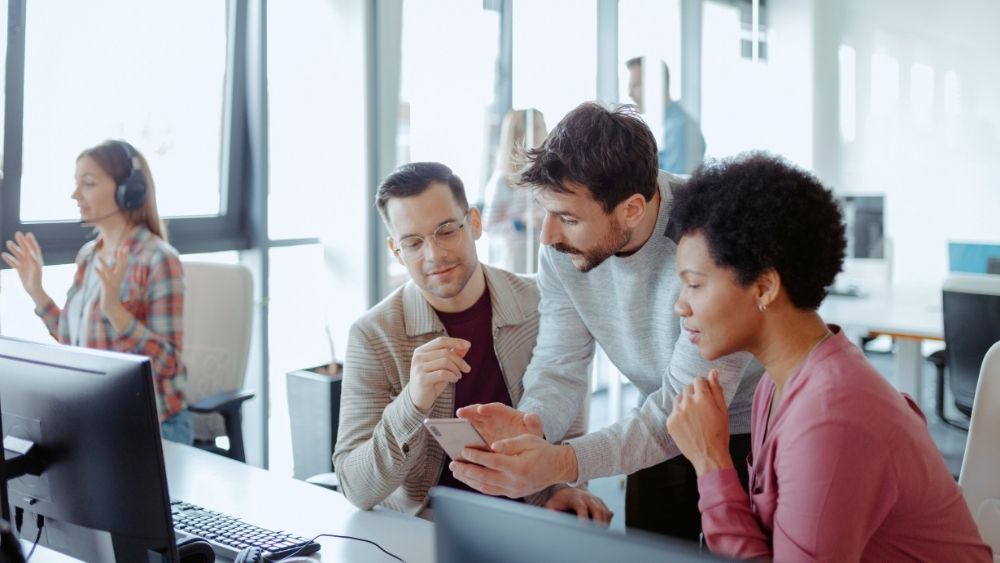 A diverse team of IT professionals collaborating at a workstation while reviewing information on a phone